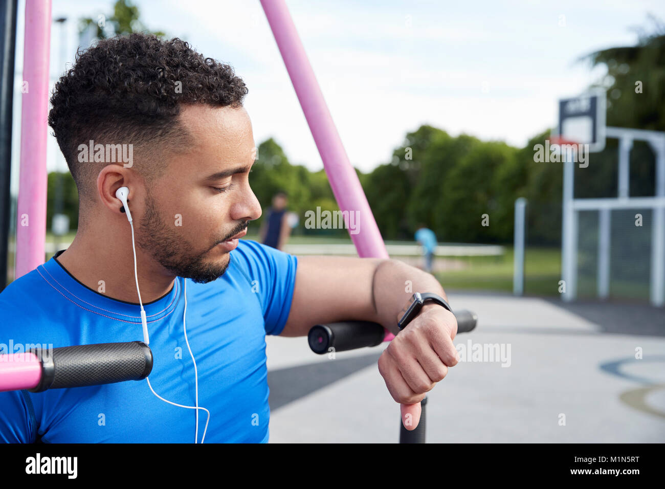 Young man at outdoor gym checking fitness app on smartwatch Stock Photo