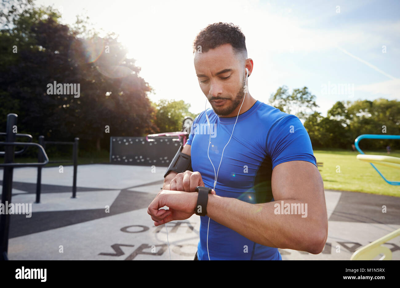 Young man at outdoor gym setting fitness app on smartwatch Stock Photo