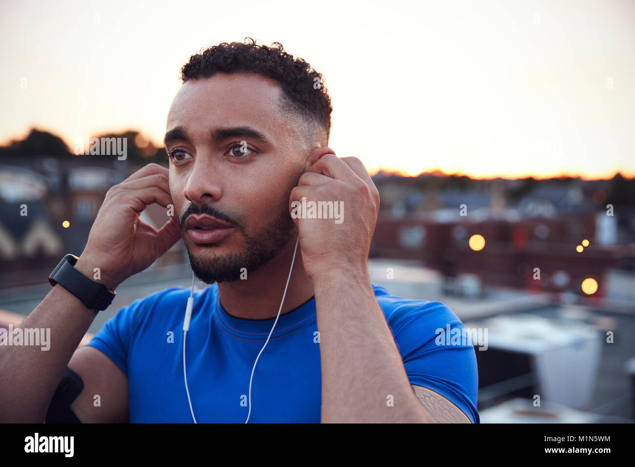 Male runner in urban setting adjusting earphones, close up Stock Photo