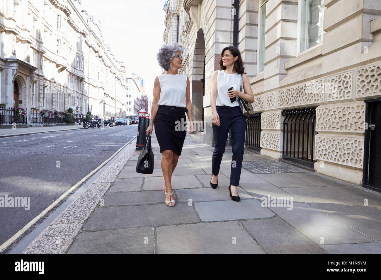 Two female colleagues walking in the street talking Stock Photo