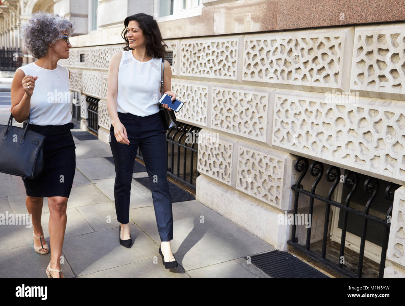 Two female work colleagues walking in the street talking Stock Photo