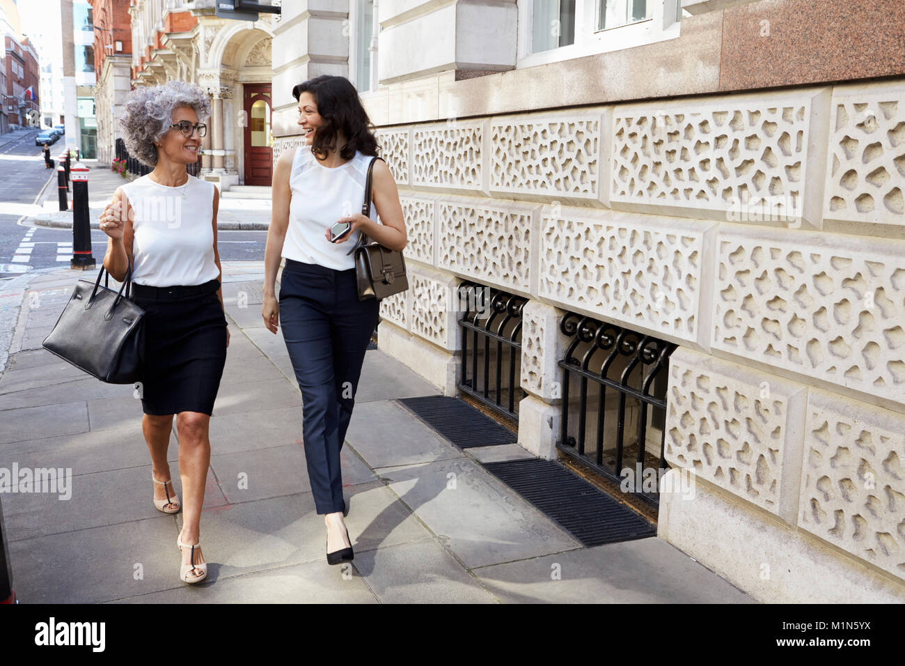 Two women walking in the street talking, full length Stock Photo