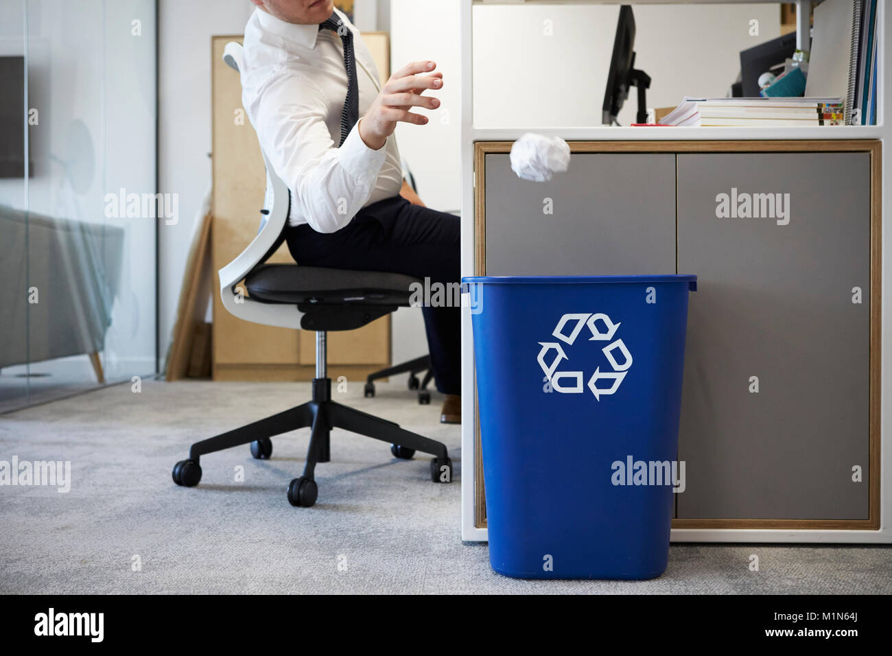 Man at desk throwing screwed up paper into recycling bin Stock Photo