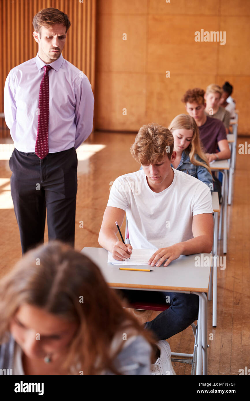 Teenage Students Sitting Examination With Teacher Invigilating Stock Photo