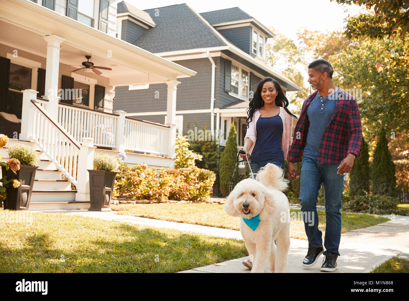 Couple Walking Dog Along Suburban Street Stock Photo