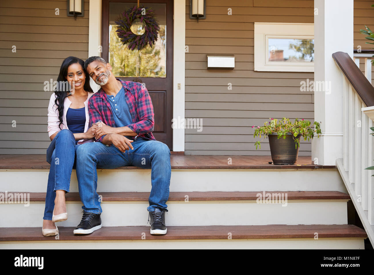 Couple Sitting On Steps Leading Up To Porch Of Home Stock Photo