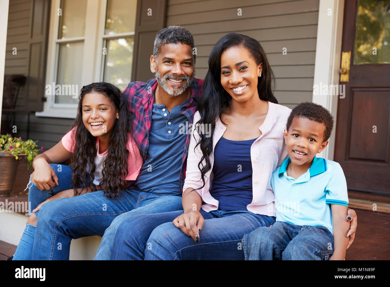 Family With Children Sit On Steps Leading Up To Porch Of Home Stock Photo