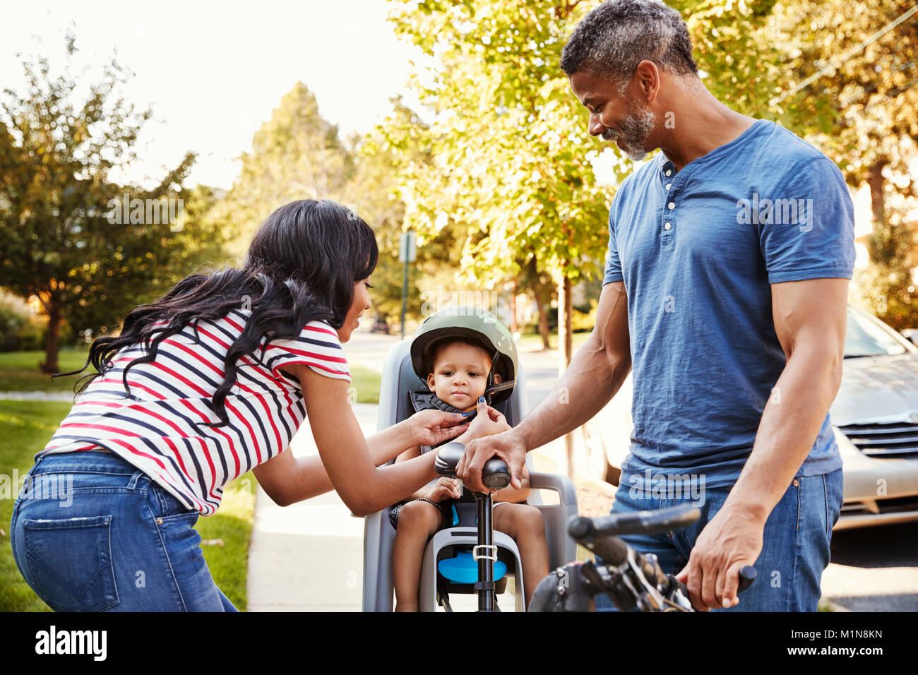 Parents Putting Daughter Into Child Seat For Bike Ride Stock Photo