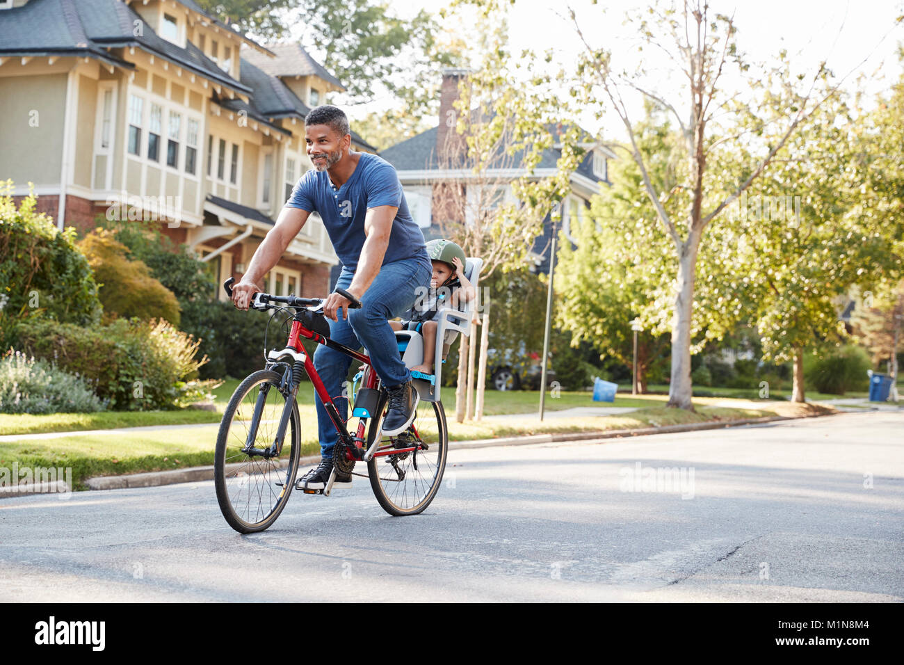 Father Cycling Along Street With Daughter In Child Seat Stock Photo