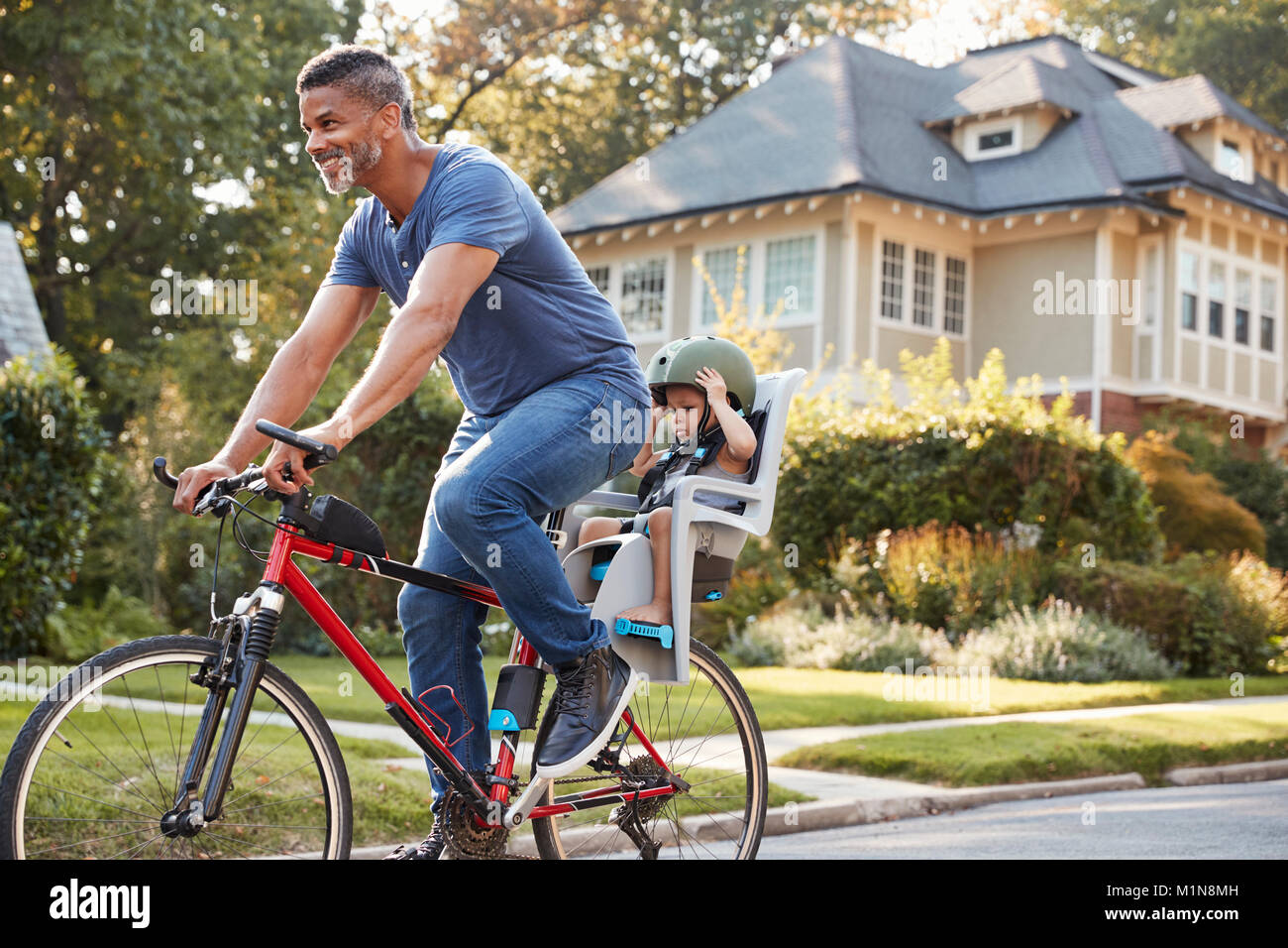 Father Cycling Along Street With Daughter In Child Seat Stock Photo