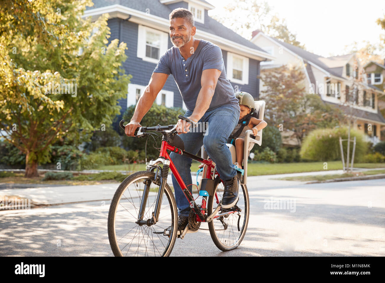 Father Cycling Along Street With Daughter In Child Seat Stock Photo