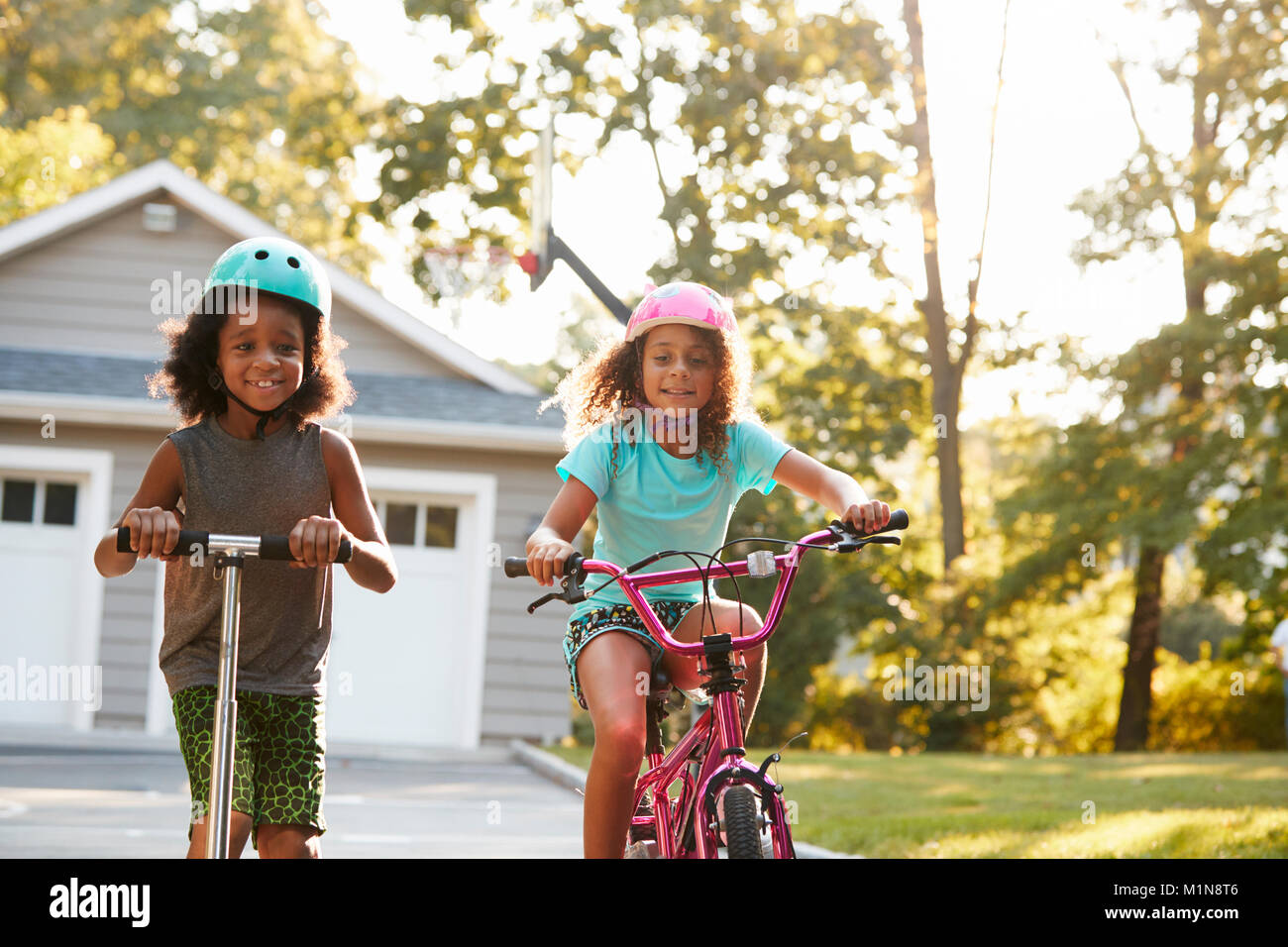 Sister With Brother Riding Scooter And Bike On Driveway At Home Stock Photo