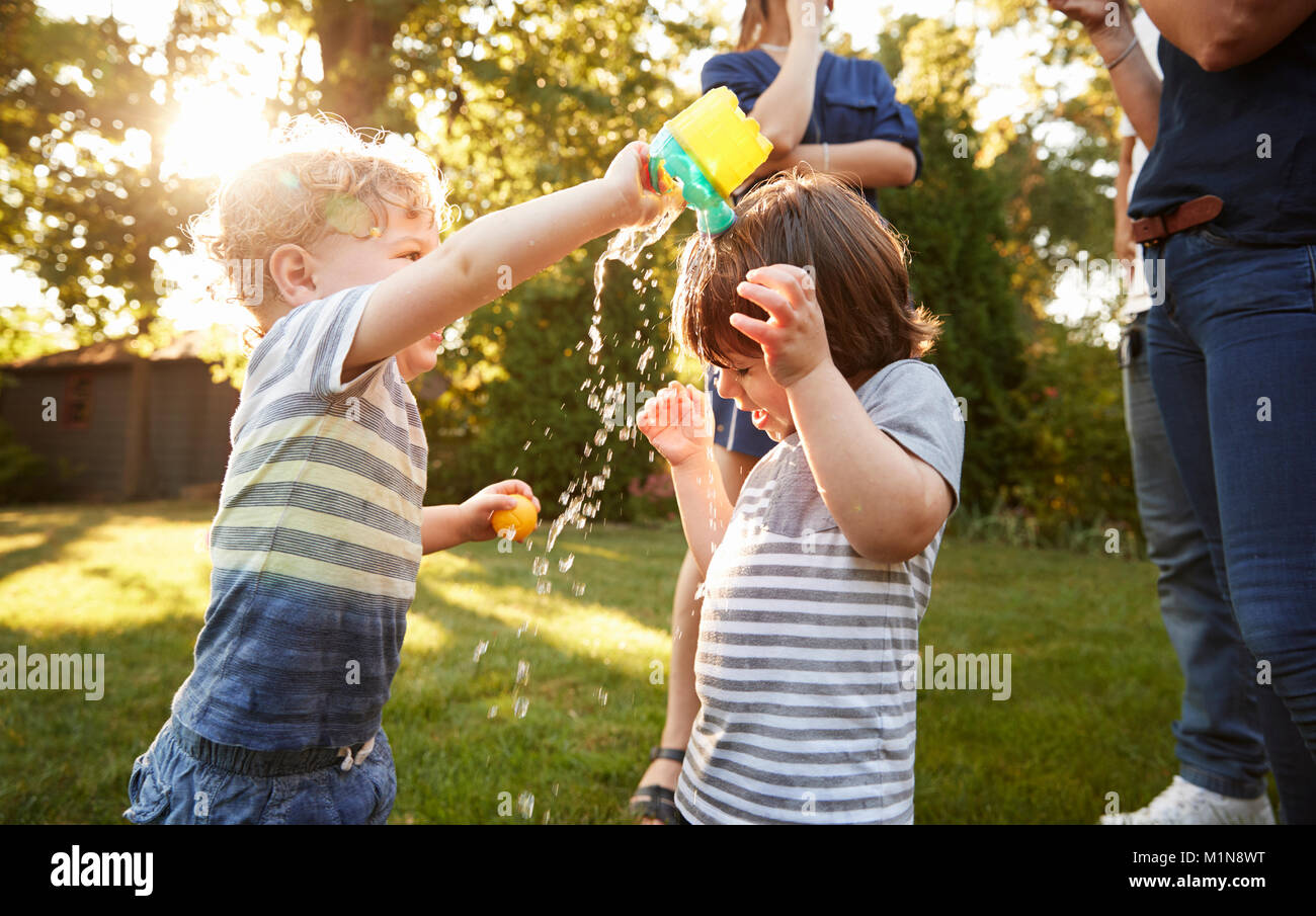 Boy Pouring Water Over Friends Head In Garden Stock Photo