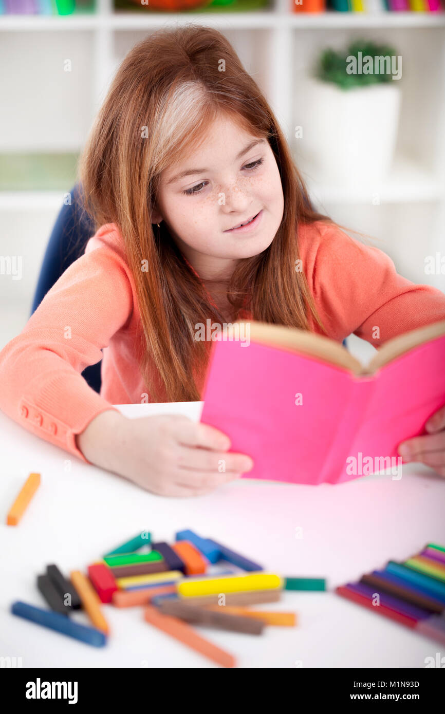 cute little red-haired girl reading a book at home Stock Photo