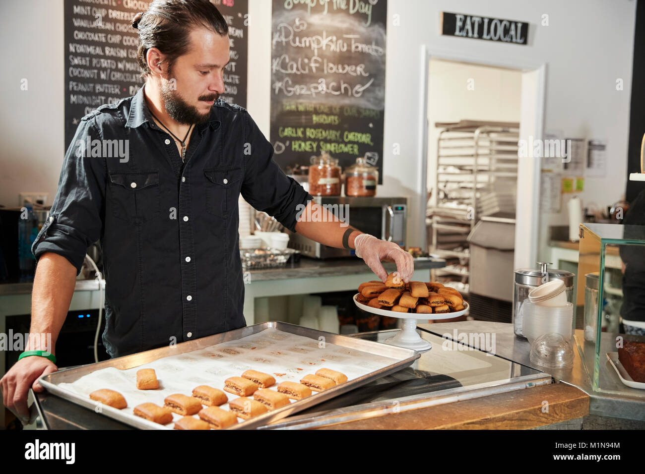 Waiter Behind Counter In Coffee Shop Arranging Cookie Display Stock Photo