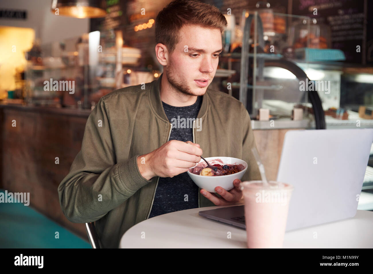 Young Man Using Laptop In Cafe Whilst Eating Breakfast Stock Photo