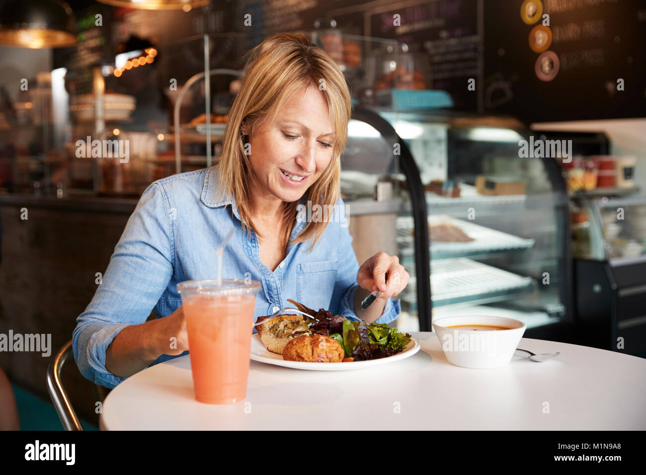 Woman In Coffee Shop Sitting At Table Eating Healthy Lunch Stock Photo