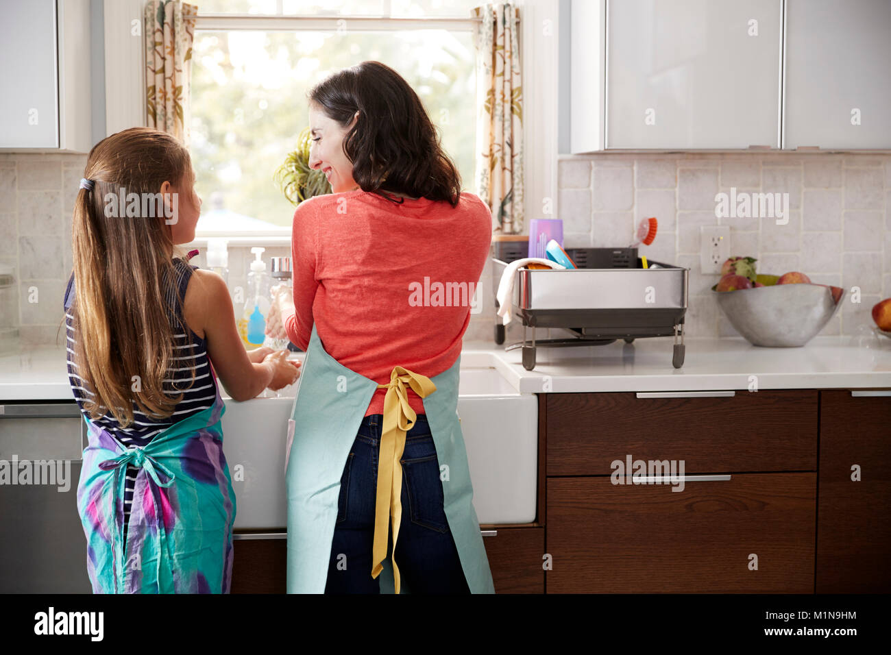 Mum and daughter washing hands at kitchen sink, back view Stock Photo