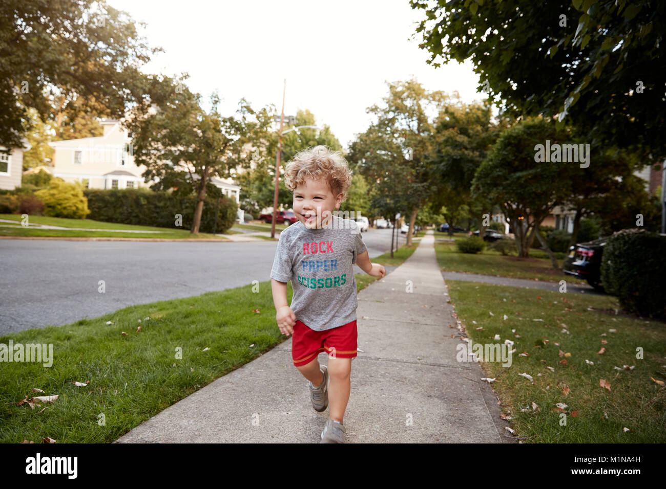 Toddler boy running in a quiet residential street Stock Photo