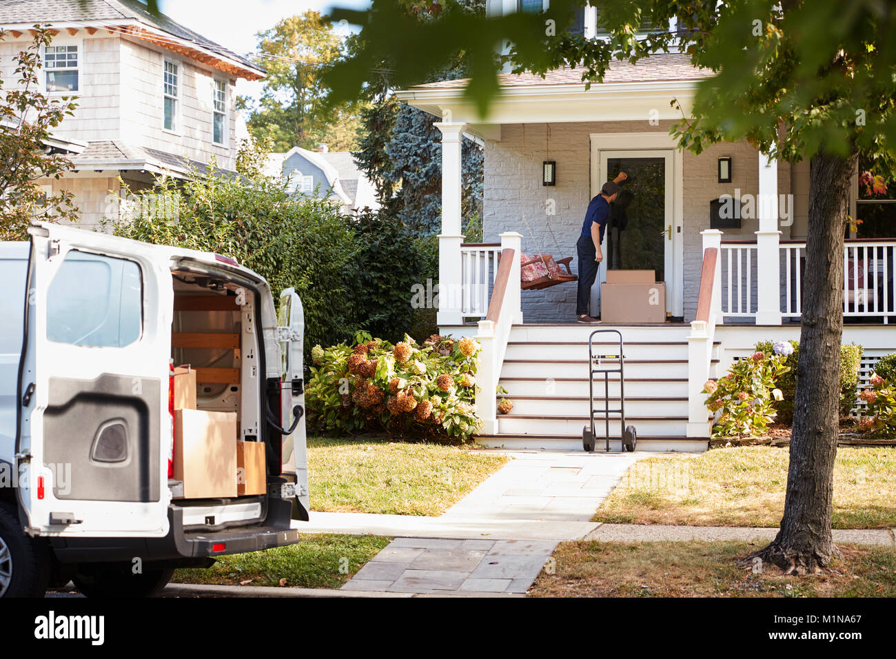 Courier Using Trolley To Deliver Package To House Stock Photo