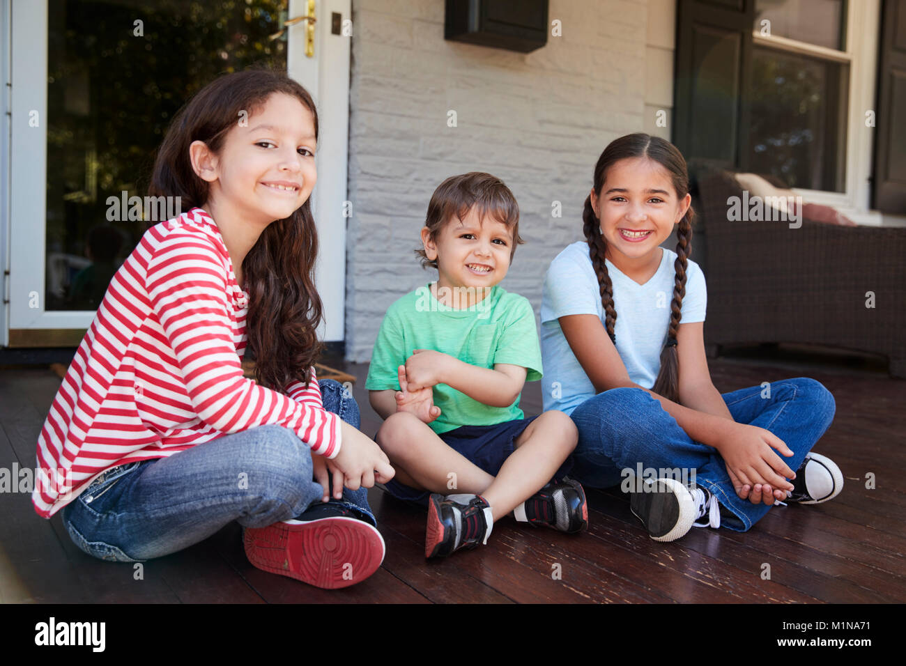 Portrait Of Children Sitting On Porch Of House Together Stock Photo