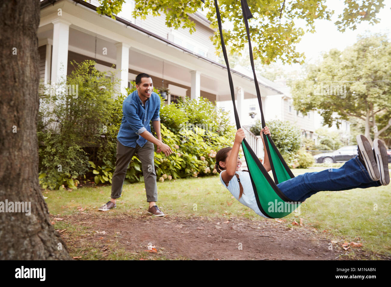 Father Pushing Daughter On Garden Swing At Home Stock Photo