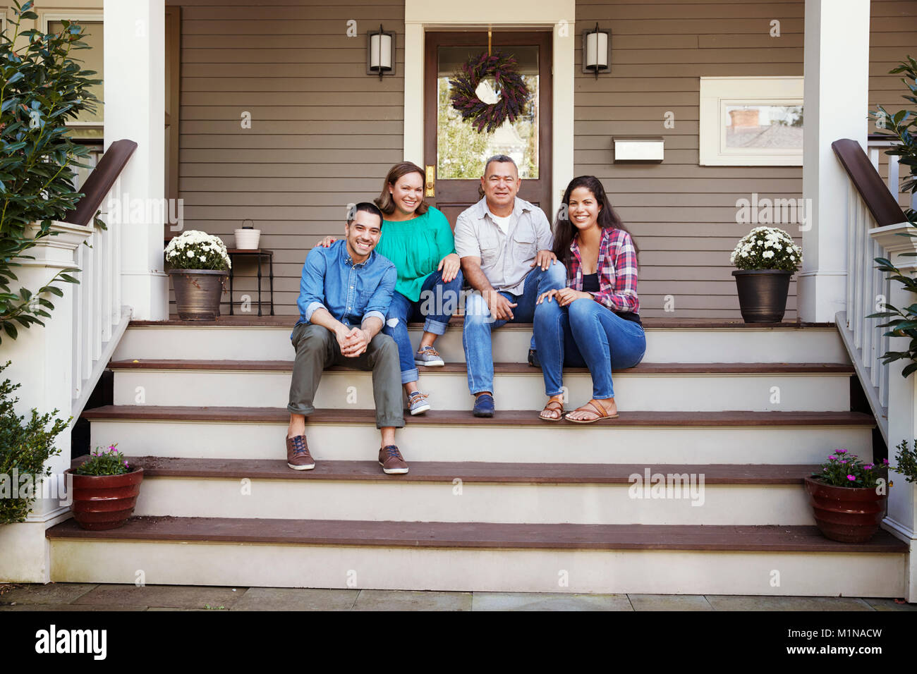 Parents With Adult Offspring Sitting On Steps in Front Of House Stock Photo