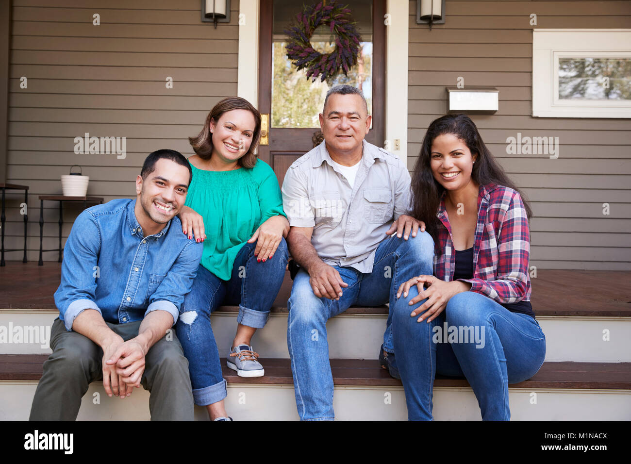 Parents With Adult Offspring Sitting On Steps in Front Of House Stock Photo