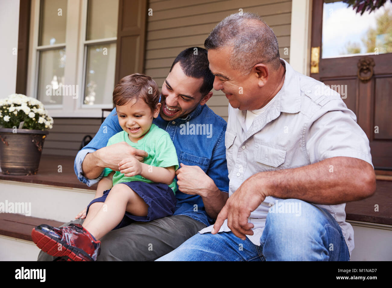 Male Multi Generation Family Sitting On Steps in Front Of House Stock Photo