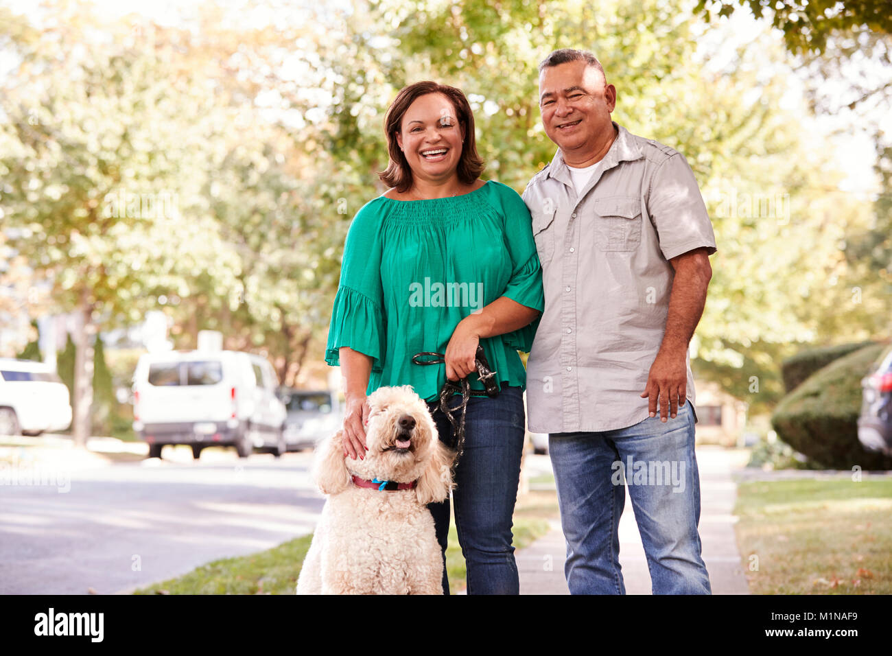 Portrait Of Senior Couple Walking Dog Along Suburban Street Stock Photo