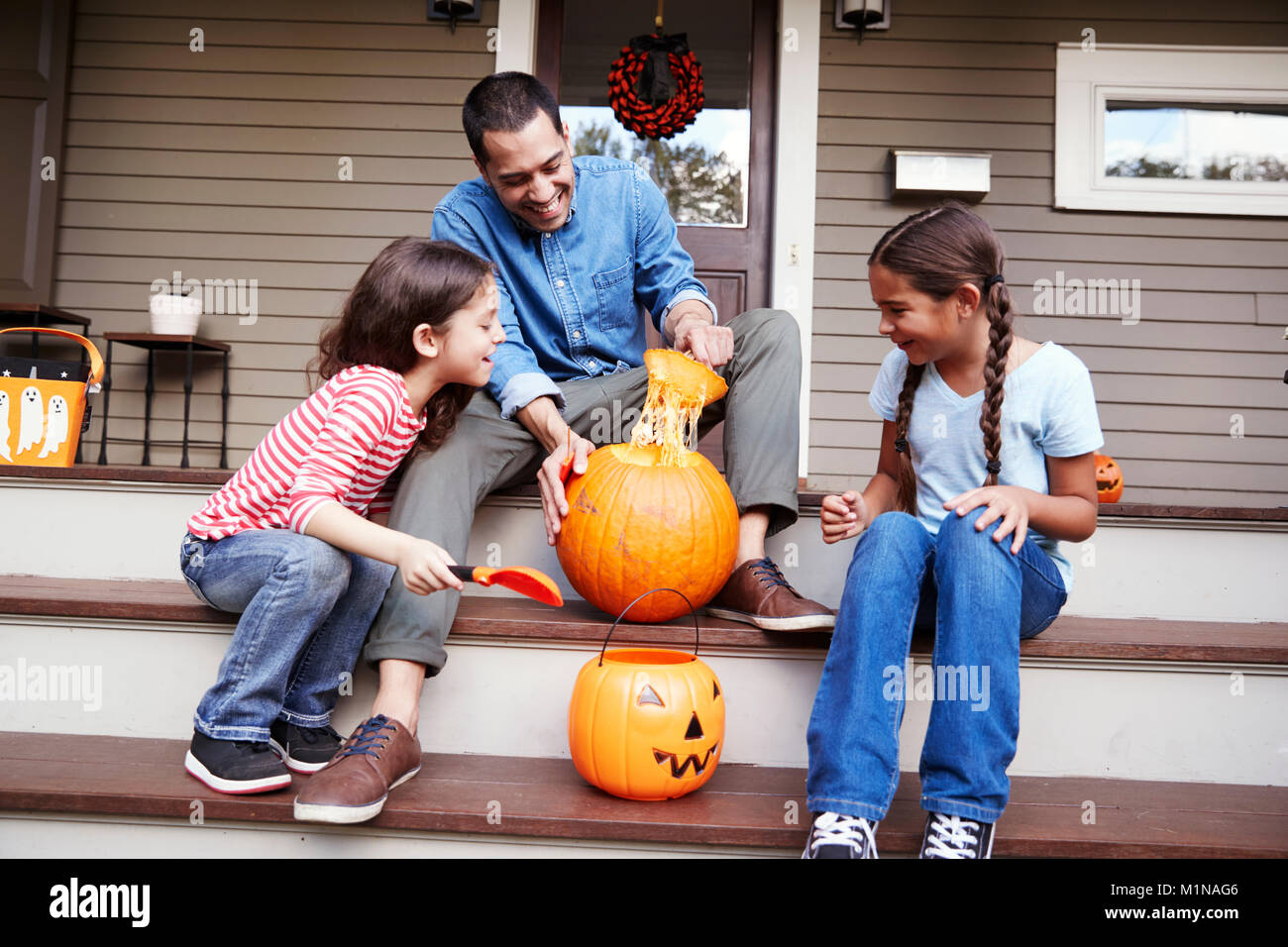 Father And Daughters Carving Halloween Pumpkin On House Steps Stock Photo