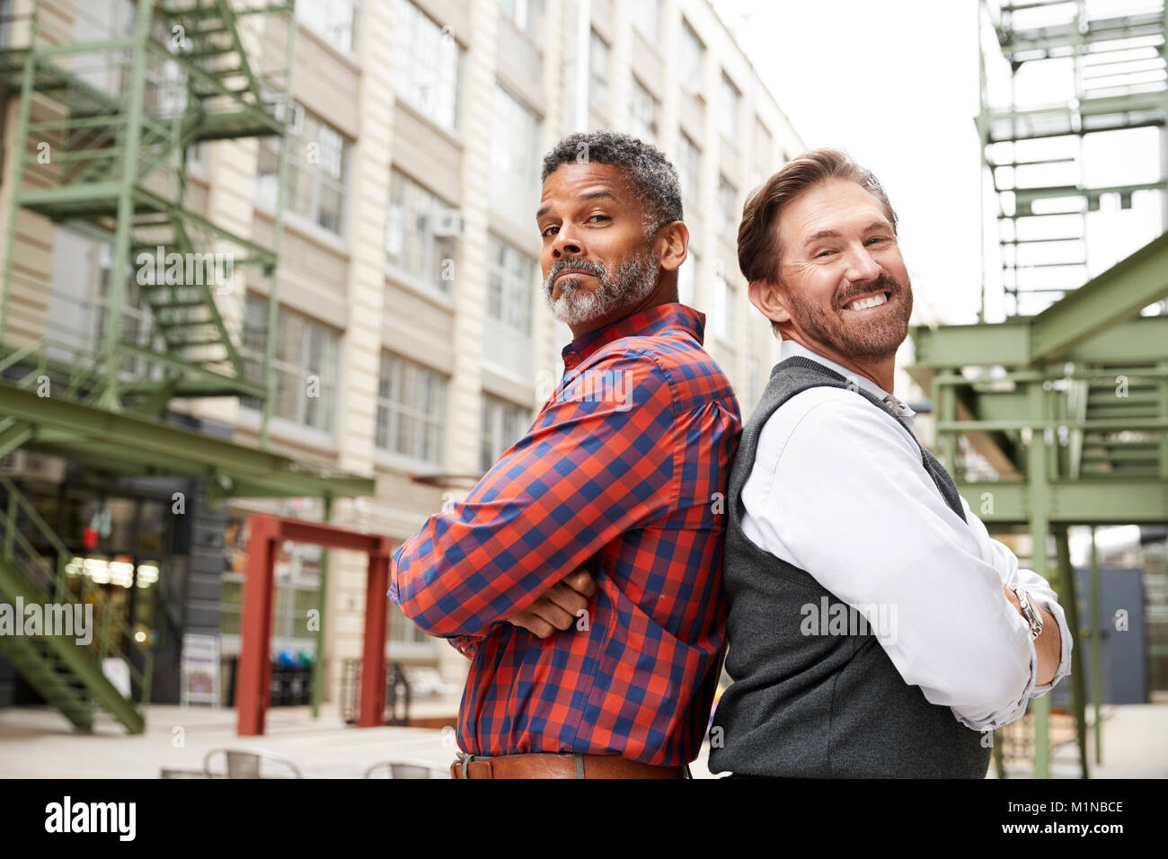 Two middle aged men stand back to back outside workplace Stock Photo