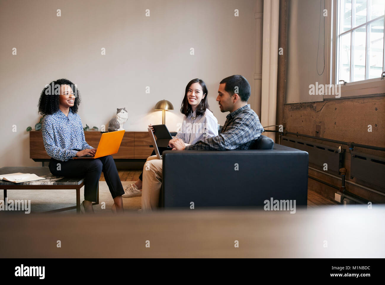 Smiling work colleagues using laptops at a casual meeting Stock Photo ...