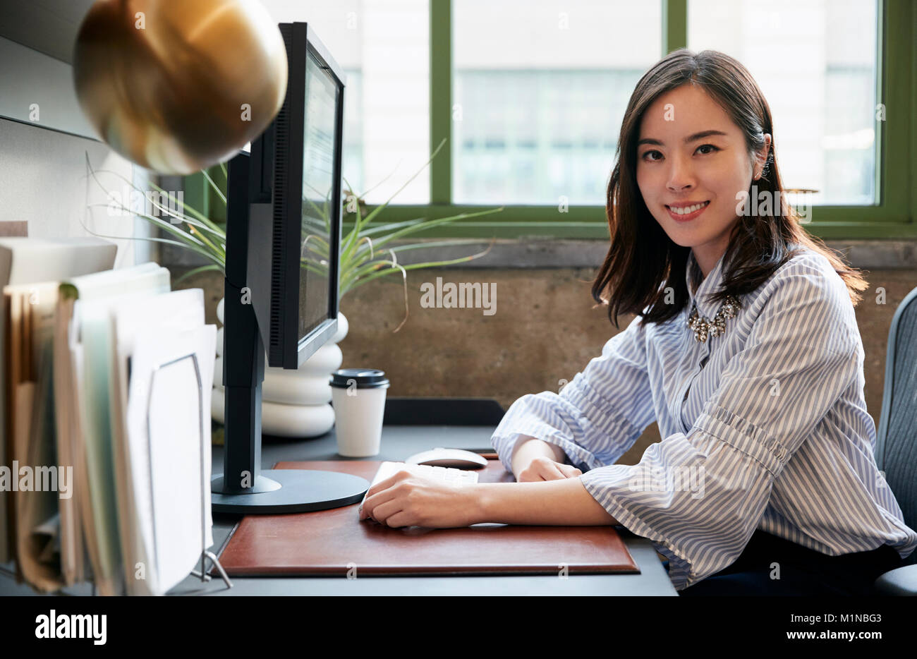 Chinese woman at a computer in an office smiling to camera Stock Photo