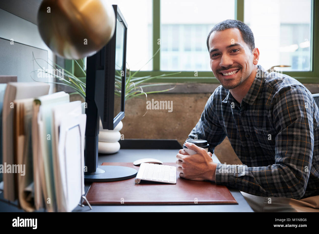 Hispanic man at a computer in an office smiling to camera Stock Photo