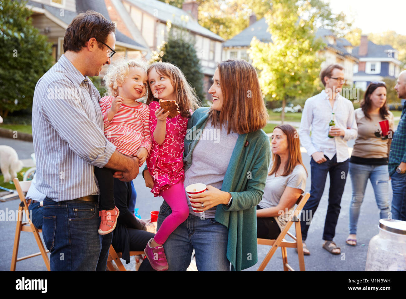 Parents holding their young kids while they eat at a block party Stock Photo