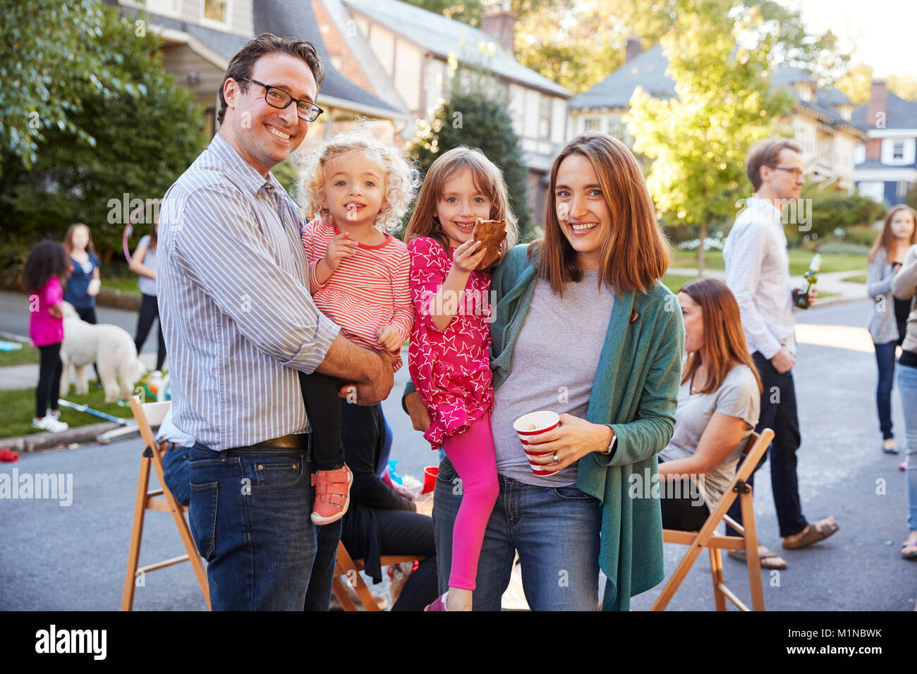 Parents holding young kids smile to camera at a block party Stock Photo