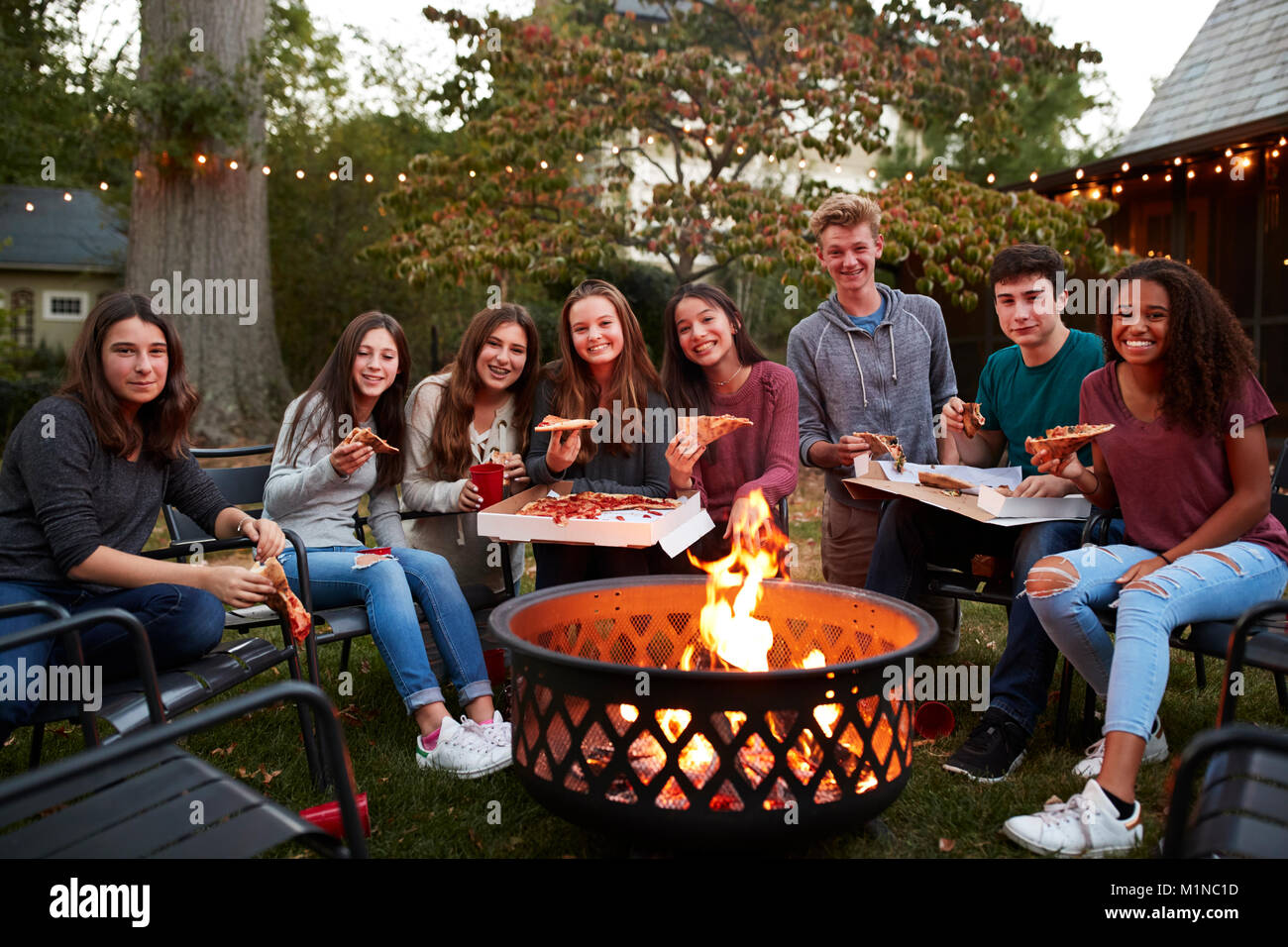 Teenagers at a fire pit with take-away pizzas look to camera Stock Photo