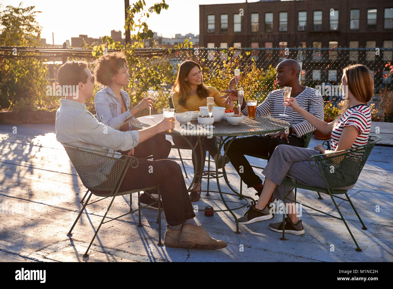 Friends talking on a New York rooftop raise glasses Stock Photo