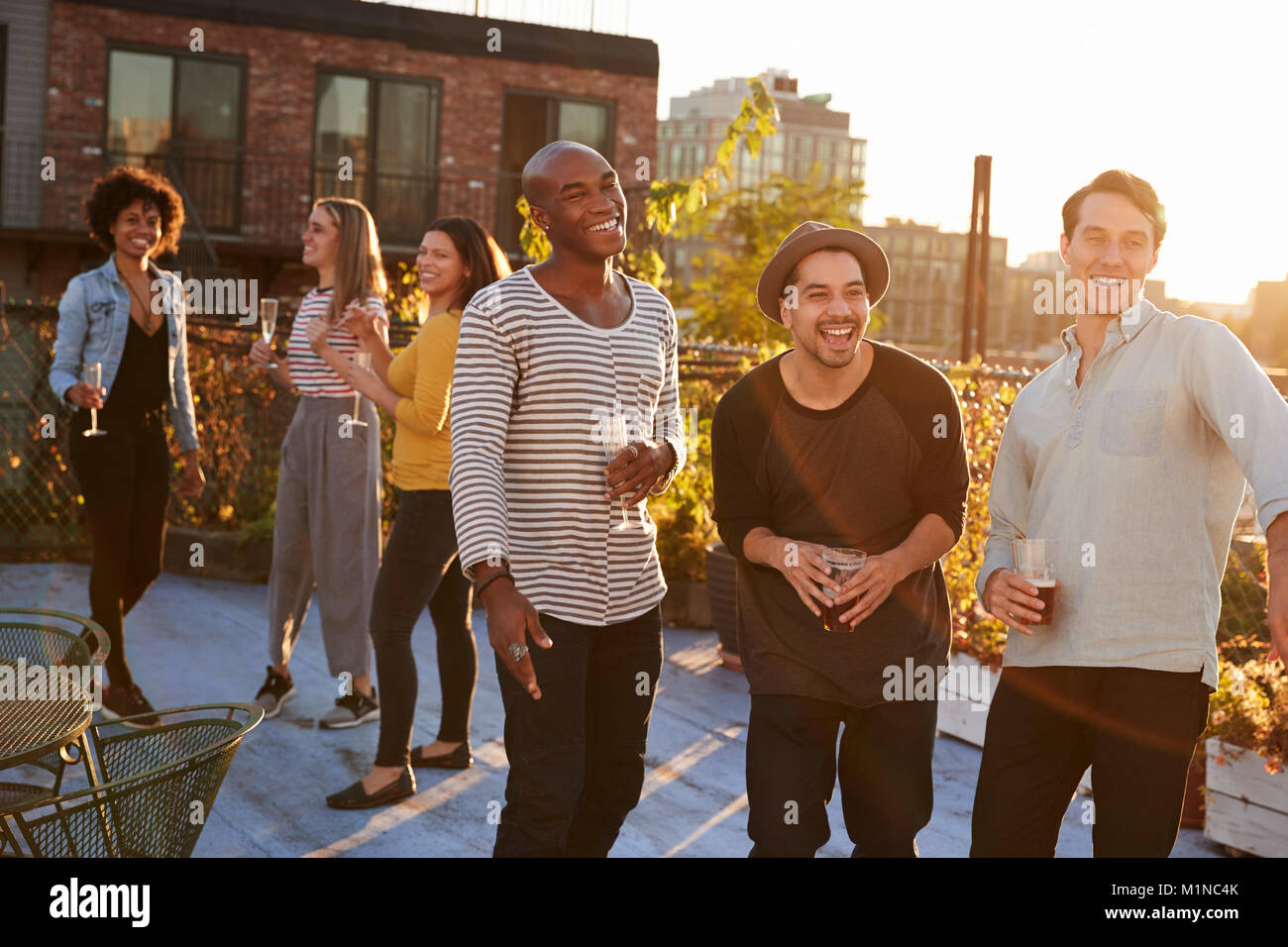 Three male friends laughing and drinking at a rooftop party Stock Photo