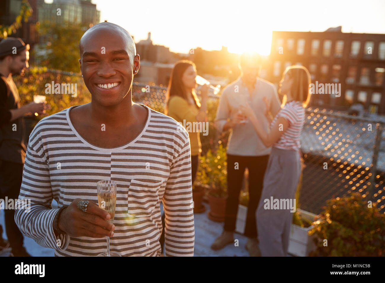 Young man holding glass at a rooftop party smiling to camera Stock Photo