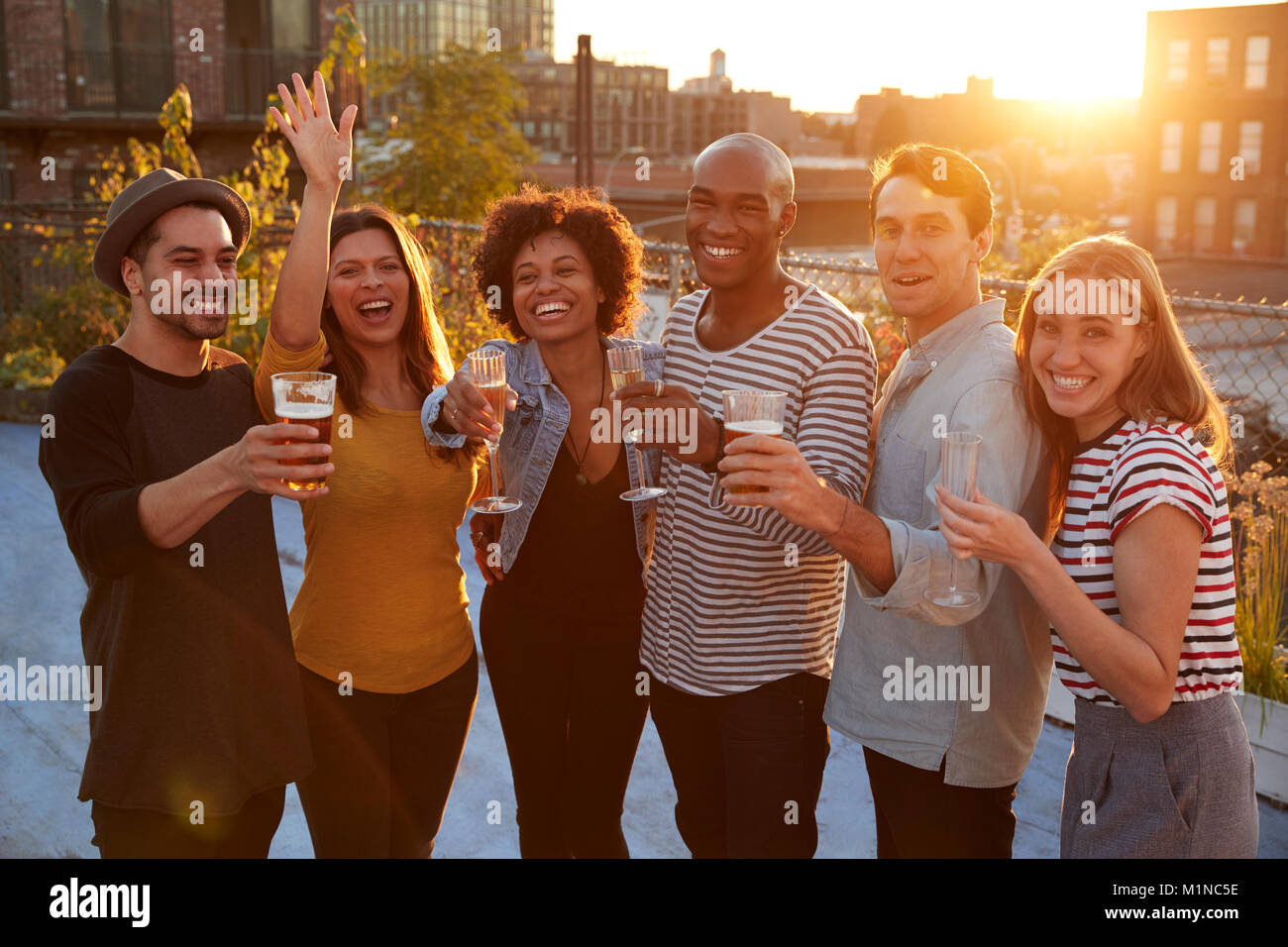 Friends at a rooftop party in raising glasses to camera Stock Photo