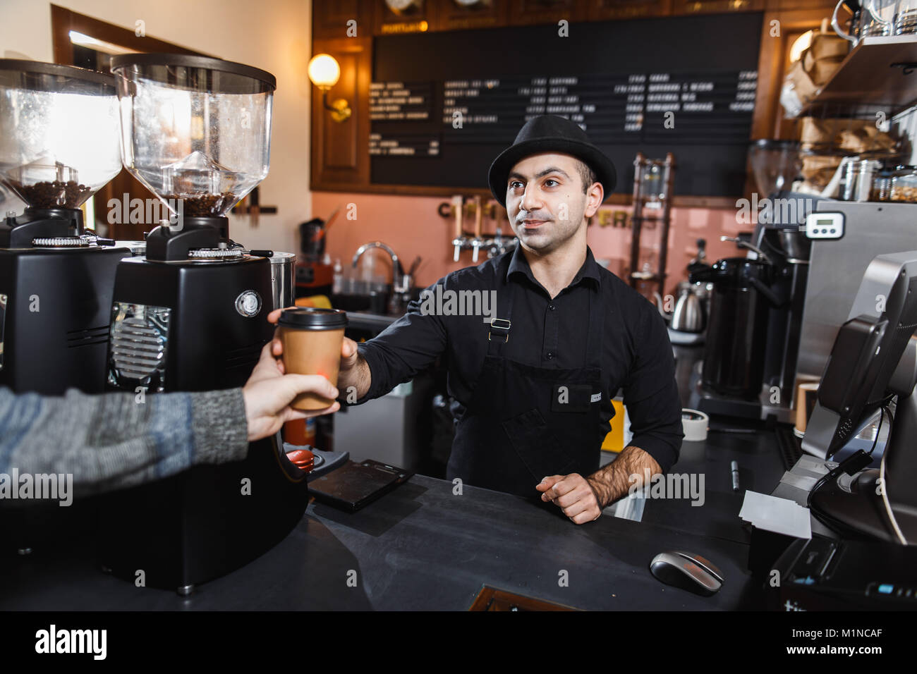 Positive barista male selling coffee to a consumer in a coffee shop