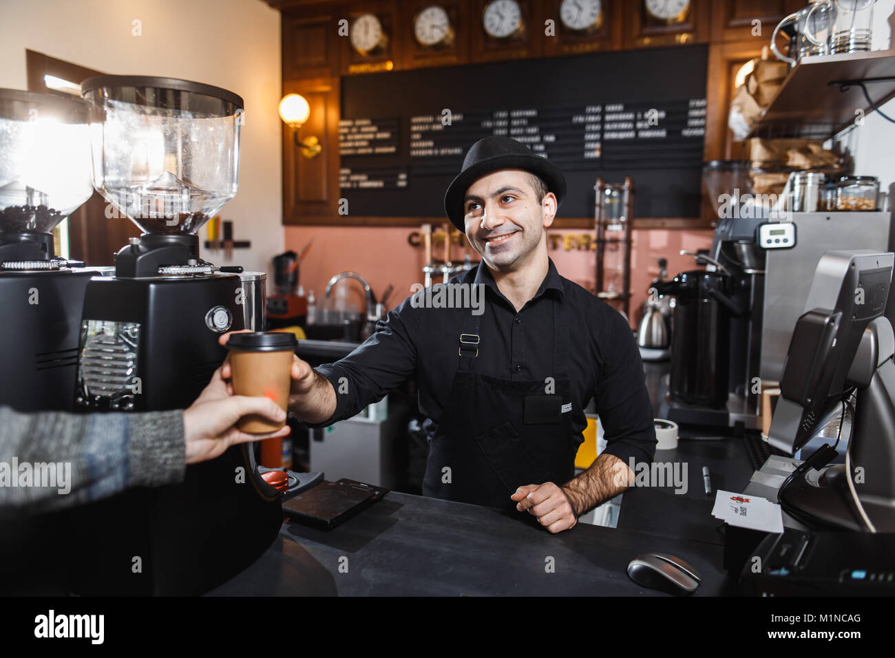Positive barista male selling coffee to a consumer in a coffee shop