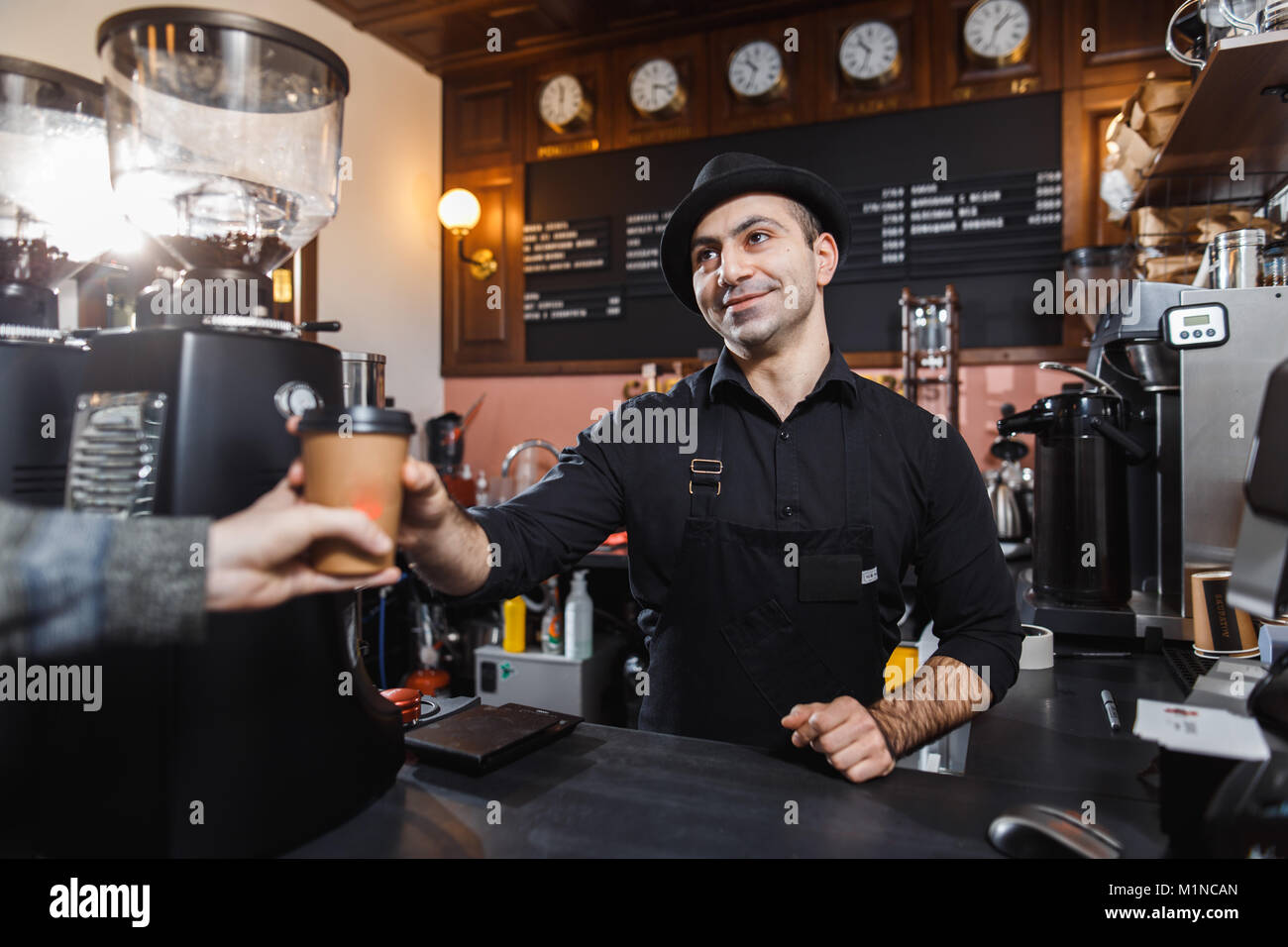 Positive barista male selling coffee to a consumer in a coffee shop