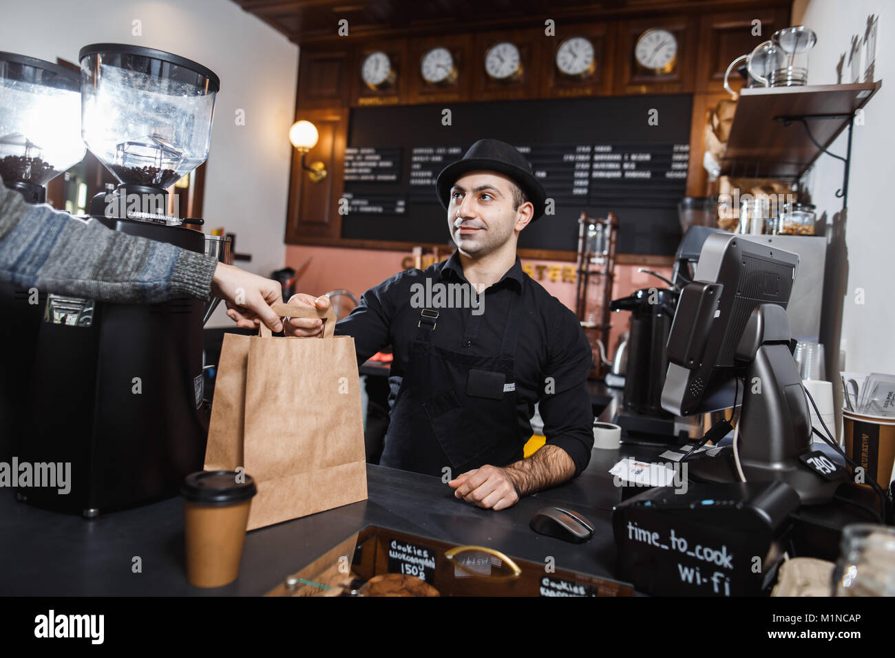 Positive barista male selling coffee to a consumer in a coffee shop