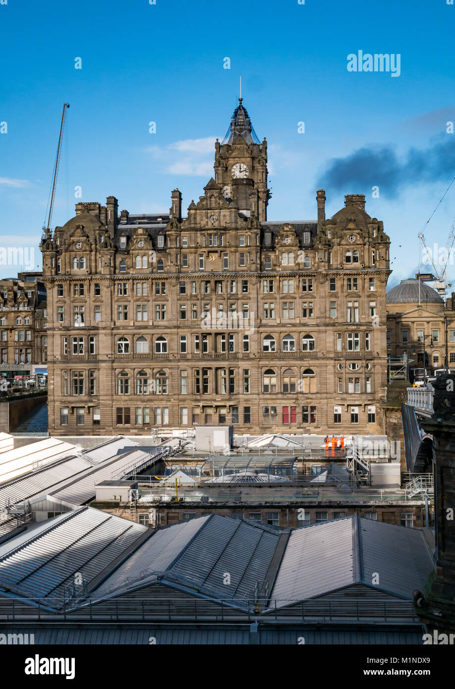 Rocco Forte Balmoral Hotel, Princes Street, Edinburgh, UK, with Waverley Station roof in front, and blue sky, cranes in distance Stock Photo