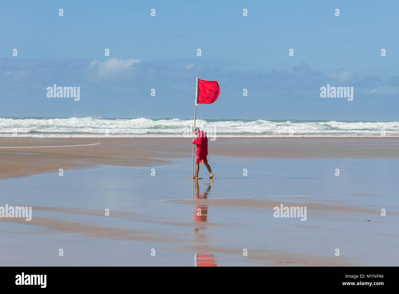 A Cornish lifeguard positioning a red flag to warn swimmers and surfers of hazardous conditions on Mawgan Porth beach, Cornwall, England, UK. Stock Photo