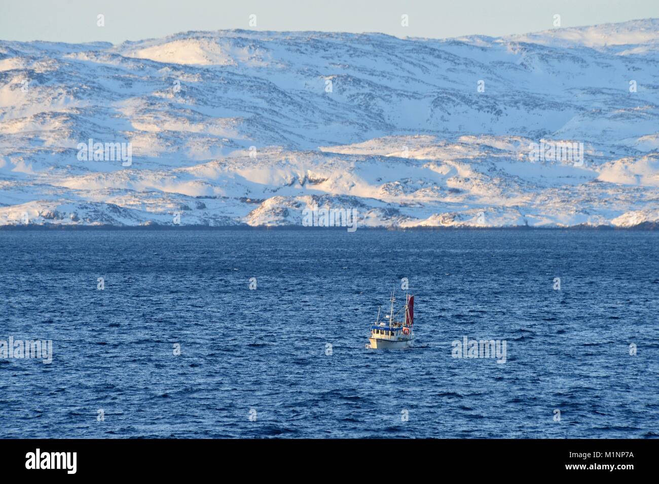 Small fishing vessel in the blue water of Varanger fjord near Vadsø with a cold coast on the horizon, 8 March 2017 | usage worldwide Stock Photo