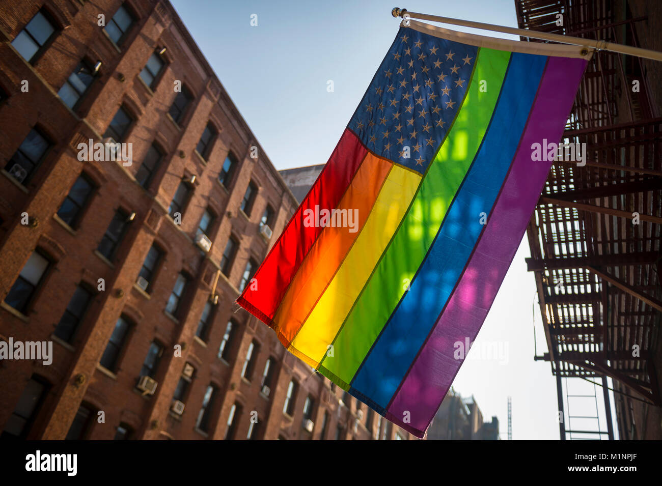 American flag with stars and gay pride rainbow stripes hanging from traditional Brooklyn building in the liberal city of New York Stock Photo